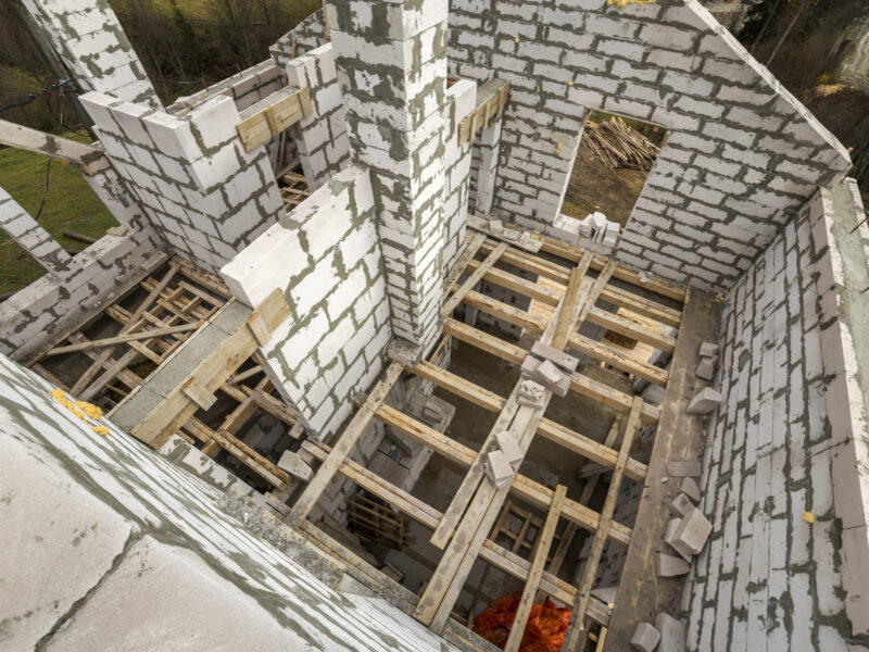 Interior of future cottage, energy saving walls of large white hollow foam insulation blocks and temporary wooden scaffolding frame. Construction, masonry, modern technology concept.
