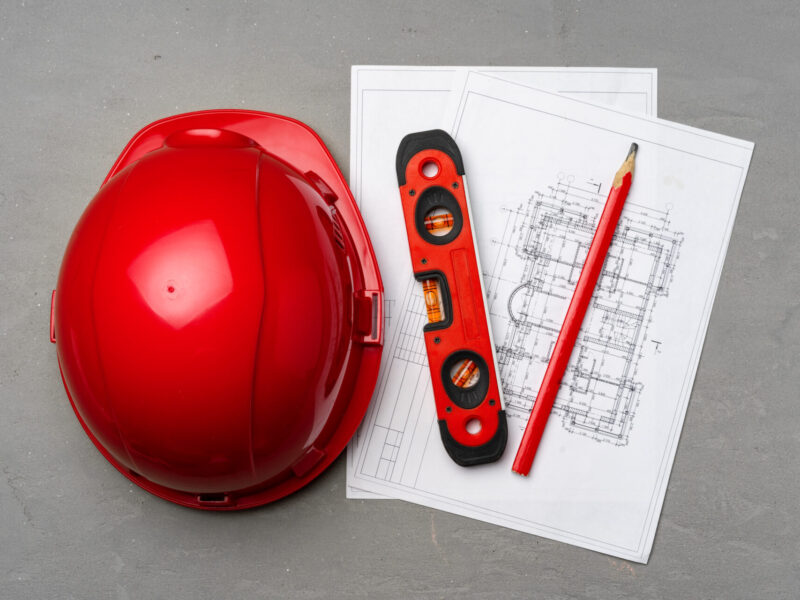 Construction worker hardhat, blueprints and .construction level, top view on wooden background
