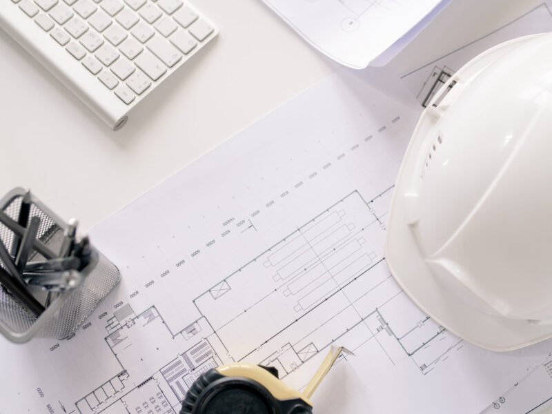 Overview of supplies of contemporary engineer on desk - hardhat, sketches, measuring tape, pencils and keypad