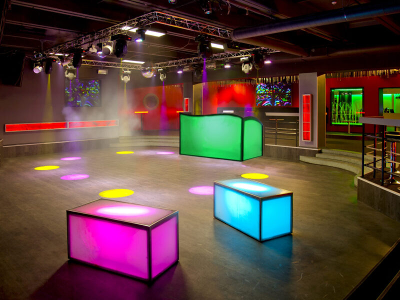 Nightclub interior, colourful lighting, wall screens and light boxes on a dance floor.