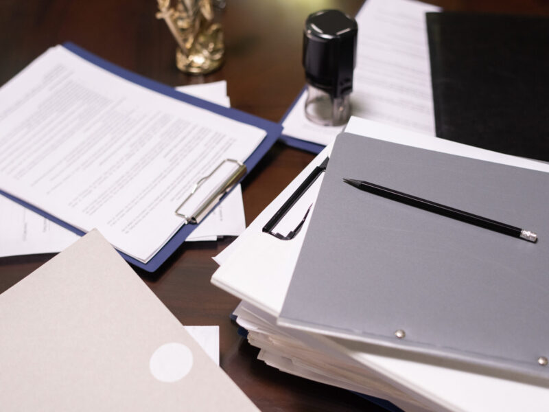 Part of table with stacks of juridical and business documents in folders and clipboards with pencil on top